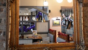 A large ornate mirror reflecting a room with hanging spherical lights, a wooden ceiling, and a brick wall. - The Boat & Horses Inn (Oldham)
