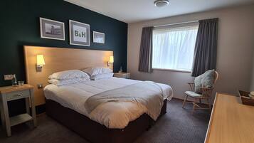 Een hotelkamer met een groot bed, nachtkastjes, een stoel, een bureau en een raam met gordijnen.