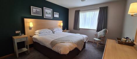 A hotel room with a large bed, bedside tables, a chair, a desk, and a window with curtains.