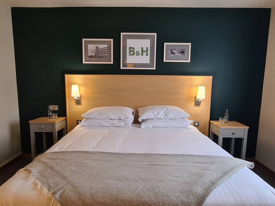 Ein ordentlich bezogenes Bett mit Kopfteil, zwei Nachttische mit Lampen und gerahmte Bilder an der Wand.