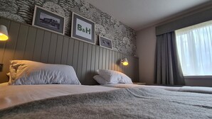A hotel room with a bed, two pillows, a wall-mounted lamp, and a window with curtains. - The Boat & Horses Inn (Oldham)