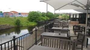 An outdoor patio with tables and chairs, a railing, and a view of a river. - The Boat & Horses Inn (Oldham)