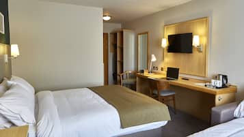 Habitación de hotel con cama, escritorio, silla, televisor y cafetera.