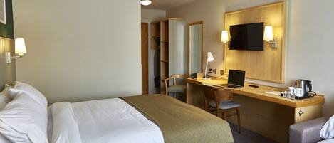 Habitación de hotel con cama, escritorio, silla, televisor y cafetera.