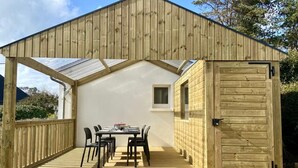 Una terraza de madera con una mesa y sillas, un espacio cubierto con una puerta y un ventanal pequeño.