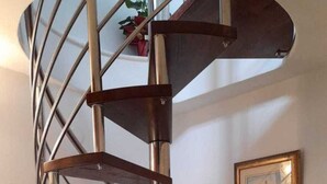Un escalier en colimaçon avec des rampes en métal et des marches en bois, menant à l’étage supérieur.