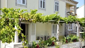 Un bâtiment à la façade blanche, doté de volets et d’une pergola recouverte de plantes grimpantes.