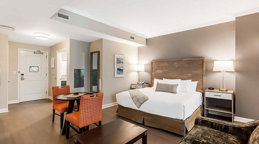 A hotel room with a bed, bedside tables, a desk with chairs, a mirror, and a door.