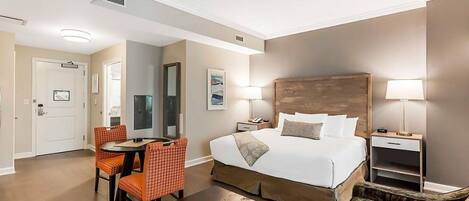 A hotel room with a bed, bedside tables, a desk with chairs, a mirror, and a door.