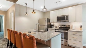 Kitchen features a central island with a sink and stove, stainless steel appliances, and pendant lights.