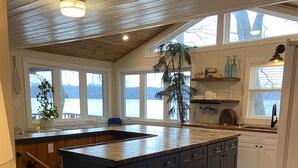 Une cuisine spacieuse dotée d’un grand îlot central, de meubles en bois et offrant une vue sur un lac grâce à de grandes fenêtres.
