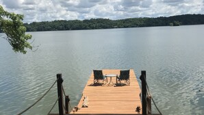 Une jetée en bois, avec deux chaises et une table, qui mène à une étendue d'eau calme.