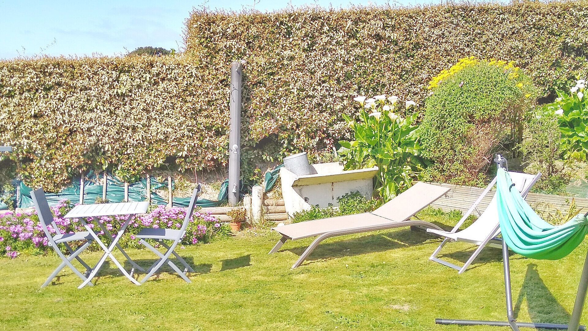 Ein Garten mit Hecke, zwei Liegestühlen, einer Hängematte und einem Tisch.