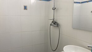 Casa de banho com paredes em azulejo branco, chuveiro com mangueira e lavatório branco com espelho em cima.