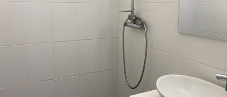 Un bagno con pareti rivestite di piastrelle bianche, una doccia con soffione a mano e un lavandino bianco con uno specchio sopra.