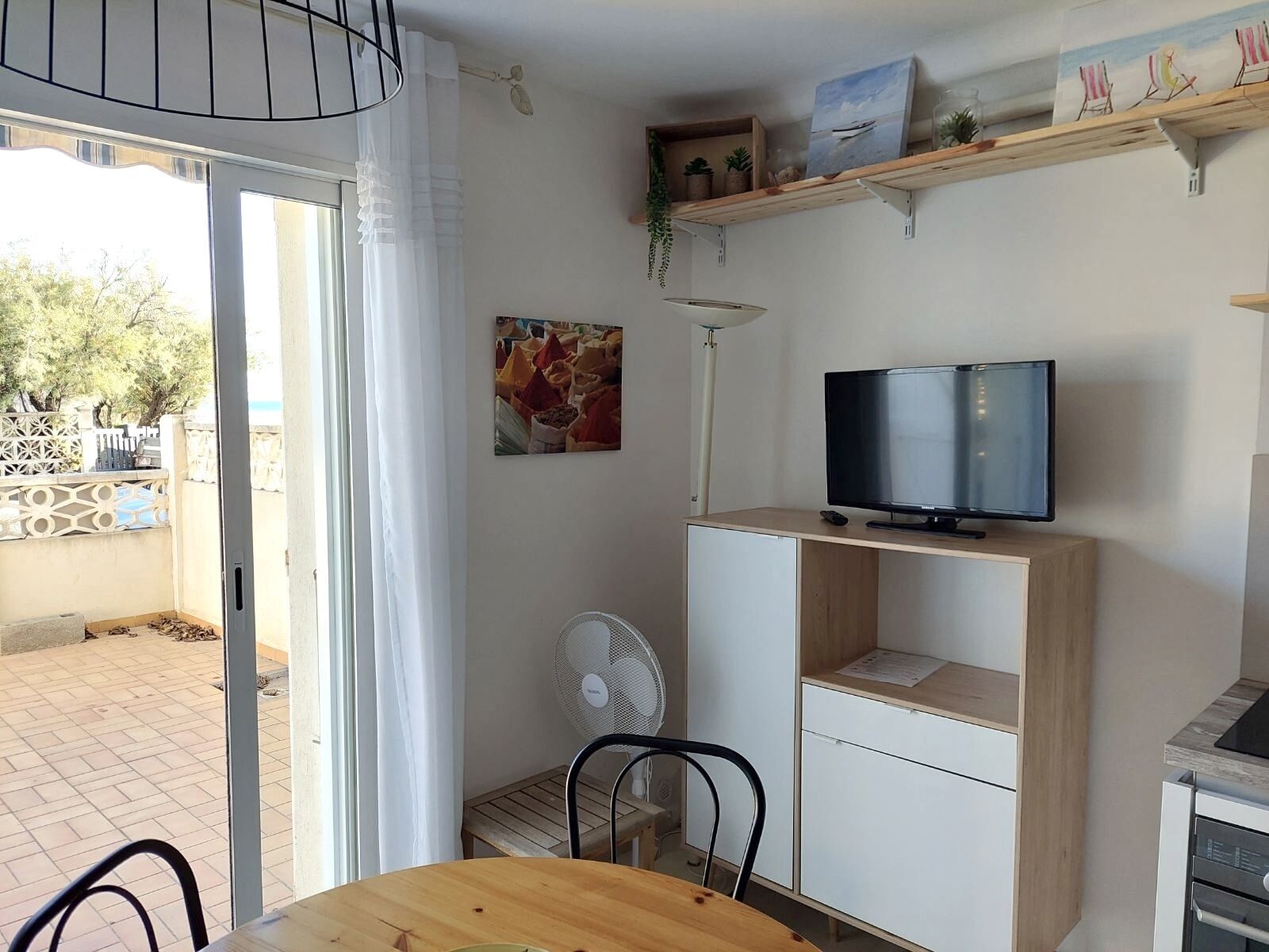 Een kamer met een televisie op een houten standaard, een ventilator en een tafel met stoelen.