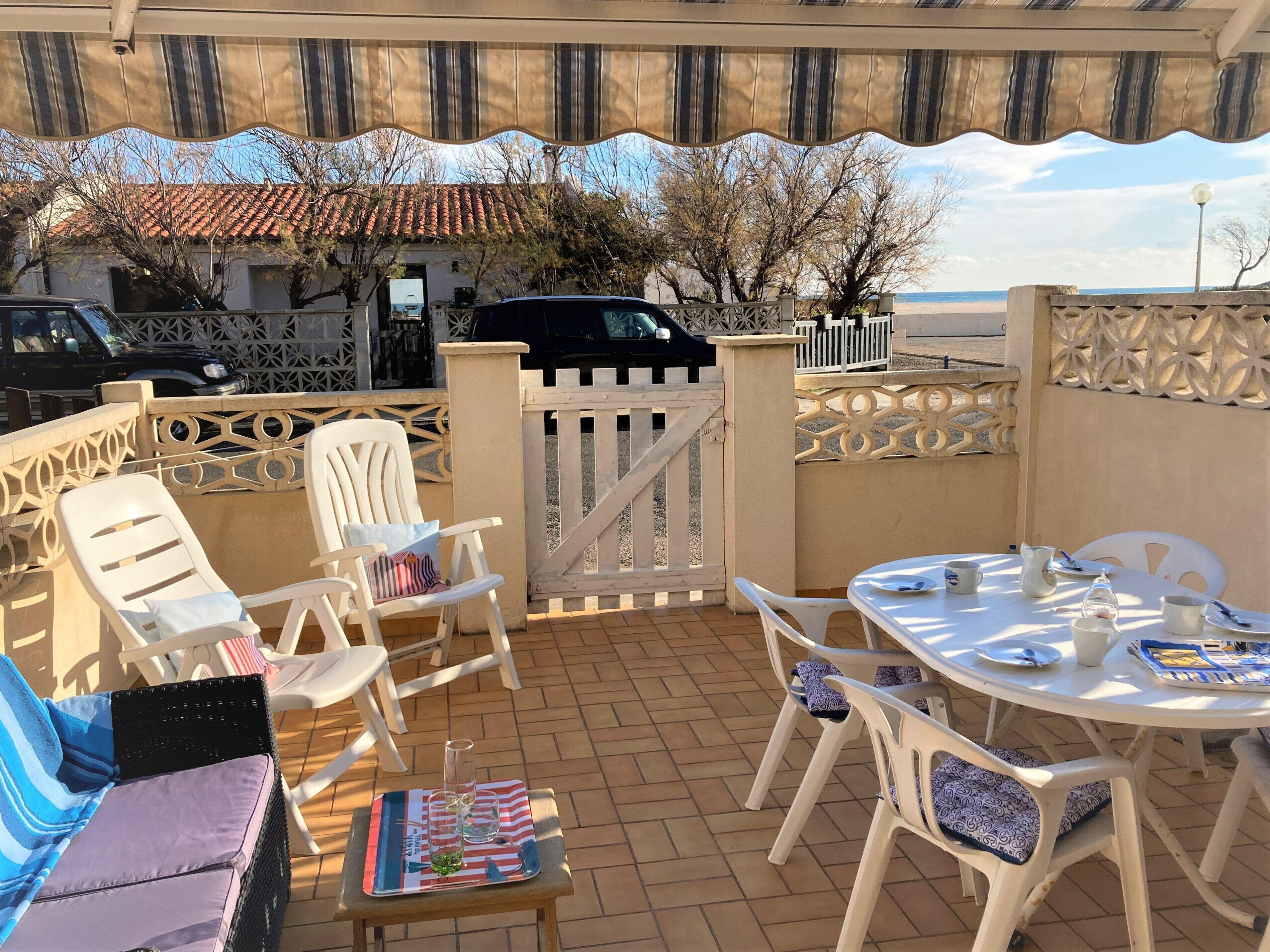 Un patio al aire libre con sillas y mesas de plástico blanco, una parrilla y vistas a la playa y al océano.