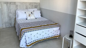 Quarto bem arrumado com cama, almofadas, cabeceira, prateleira na parede e uma pequena mesa.