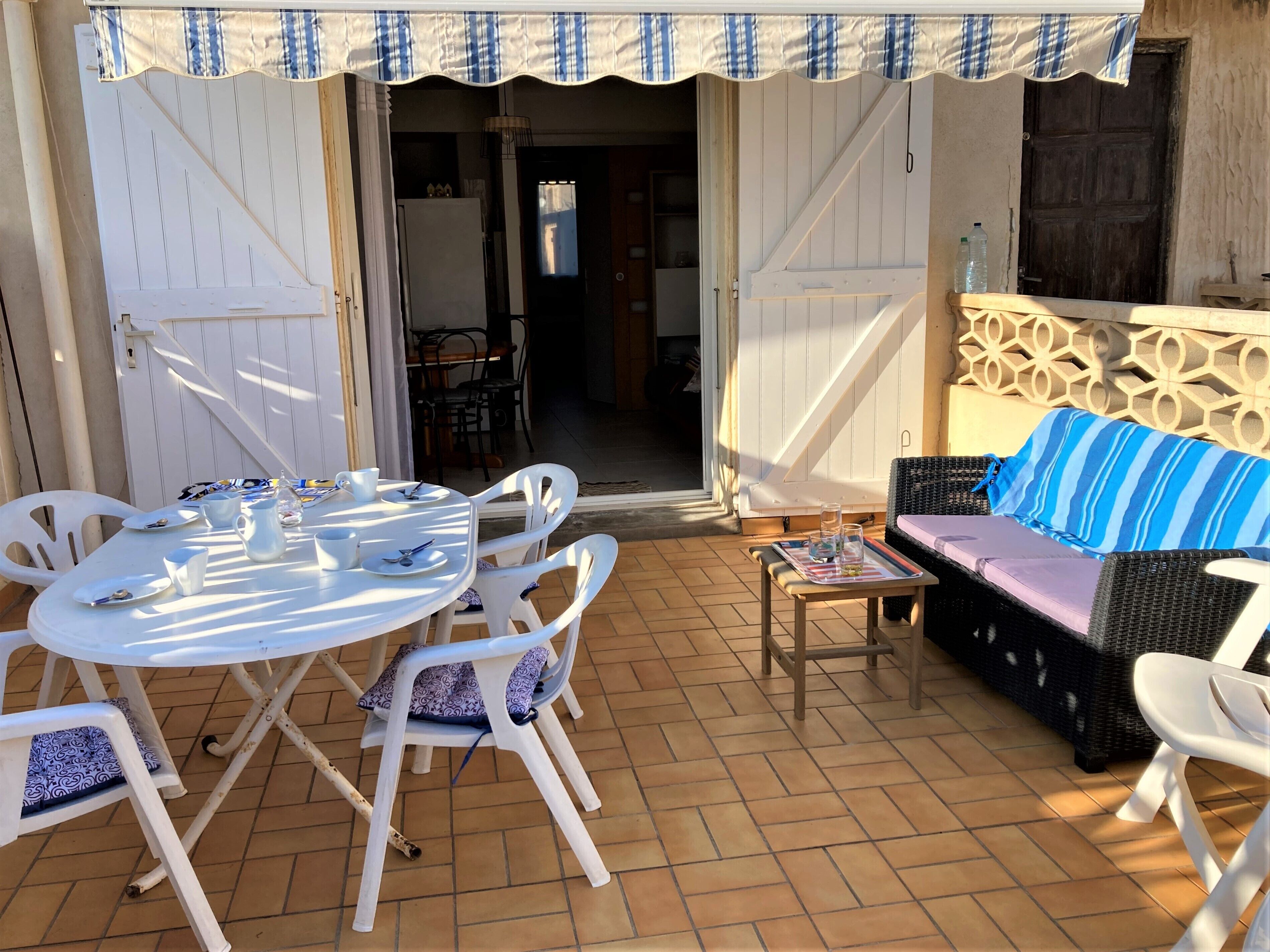 An outdoor patio with a round table, white chairs, and a sofa with a striped cushion.