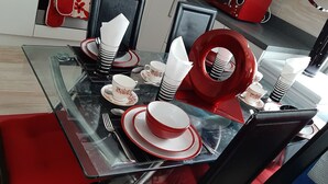 Une table à manger dressée avec des assiettes, des bols et des serviettes pliées, le tout dans des tons de rouge et de blanc.