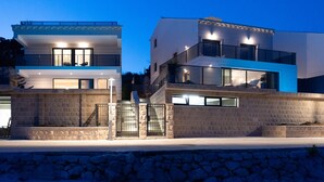 Une maison moderne à deux étages, dotée d’une façade en pierre, de grandes fenêtres et d’un balcon.