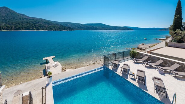 Un espace aménagé au bord de la piscine, offrant une vue dégagée sur un lac, avec des chaises longues et une montagne en arrière-plan.