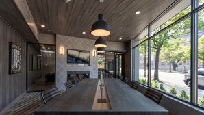 Uma sala de conferências moderna com uma mesa comprida, várias cadeiras, iluminação pendente e grandes janelas com vista para a rua.