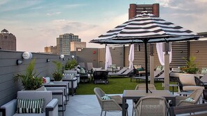 Um terraço no telhado com área de estar externa, um guarda-sol listrado e vista para a cidade.