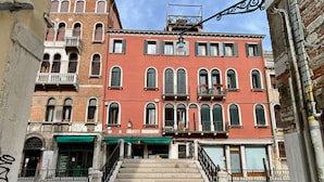Un immeuble à plusieurs étages, doté d’une façade rouge, d’un escalier menant à l’entrée et d’une marquise verte au-dessus du rez-de-chaussée.