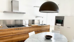 Une cuisine moderne dotée d’un îlot central, d’appareils électroménagers en acier inoxydable et d’une table ronde en marbre.