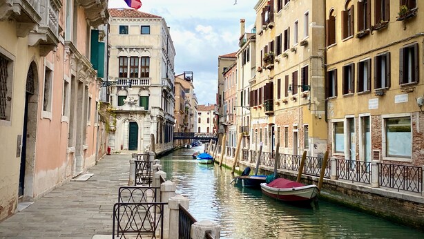 Un canal dans une ville européenne historique, bordé de bâtiments des deux côtés, avec un drapeau et des bateaux.