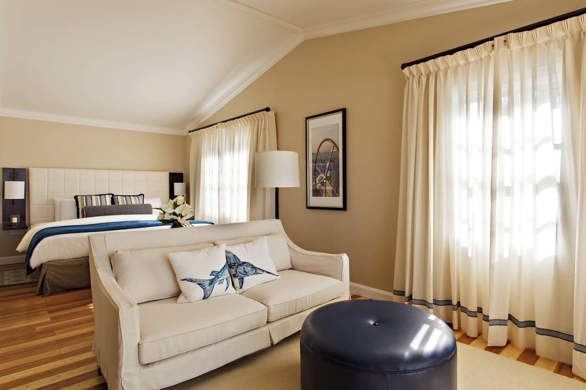 A hotel room with a bed, a sofa, a lamp, and curtains.