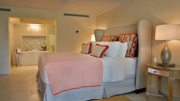 Habitación de hotel moderna con una cama grande, una mesita de noche con lámpara y un baño visible a través de una puerta abierta.