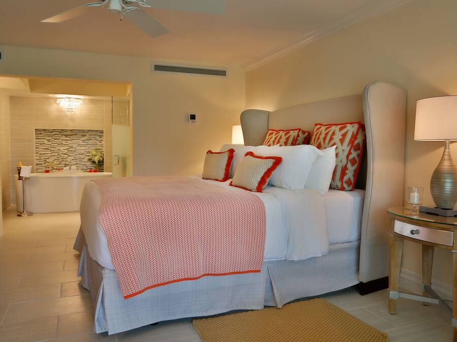 Habitación de hotel moderna con una cama grande, una mesita de noche con lámpara y un baño visible a través de una puerta abierta.