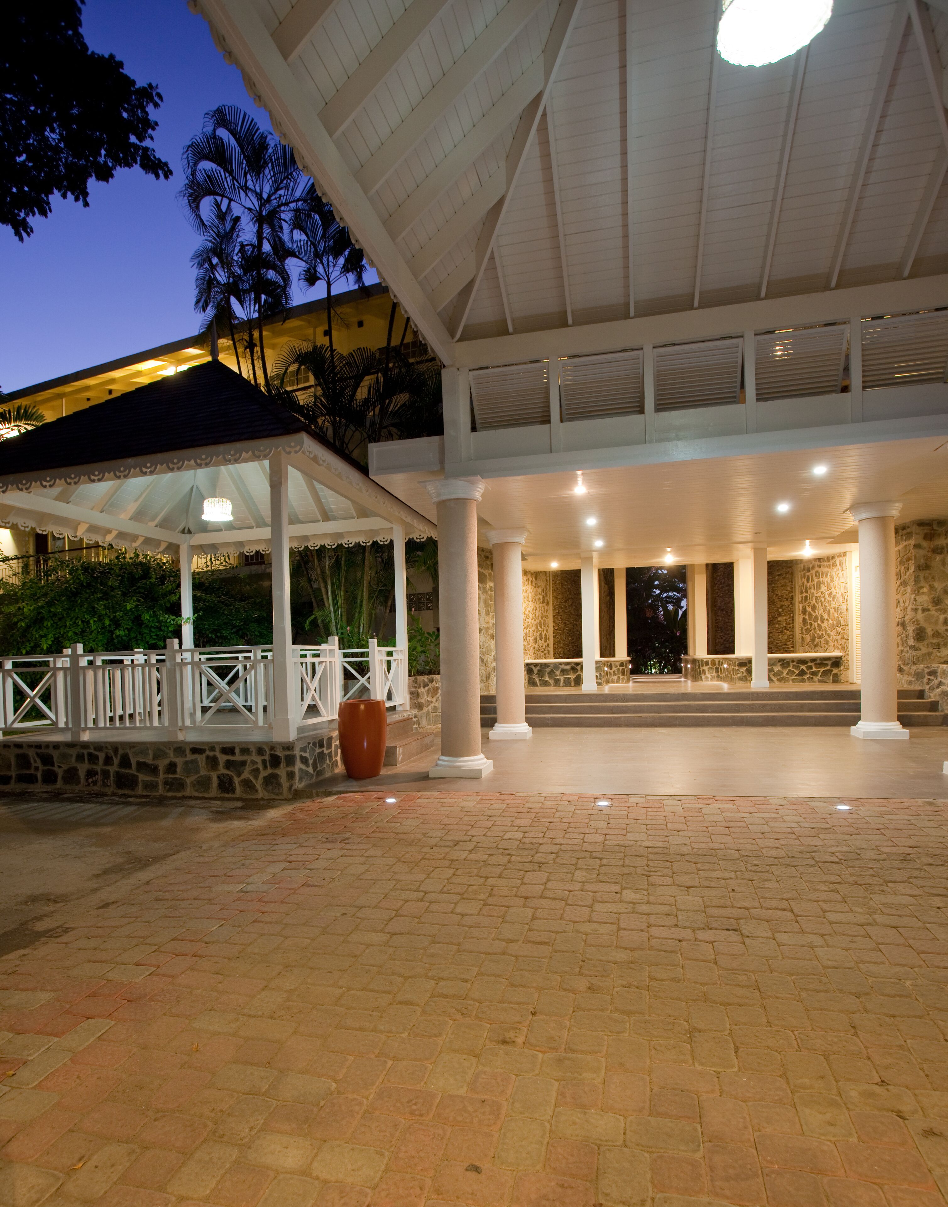 A covered outdoor area with stone columns, a white fence, and a large planter.