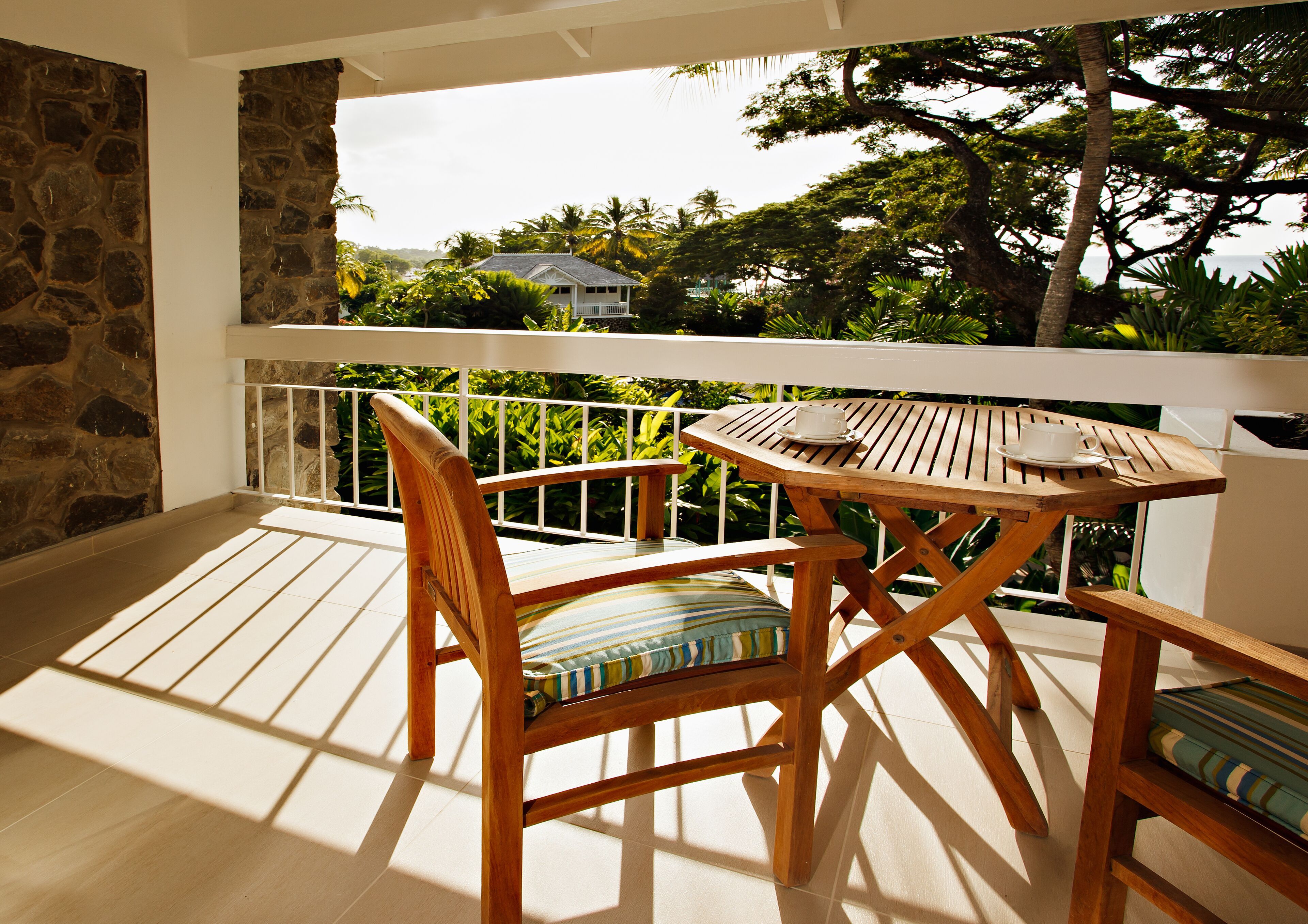 Mesa y sillas de madera en un balcón con pared de piedra y vistas a vegetación y un edificio.