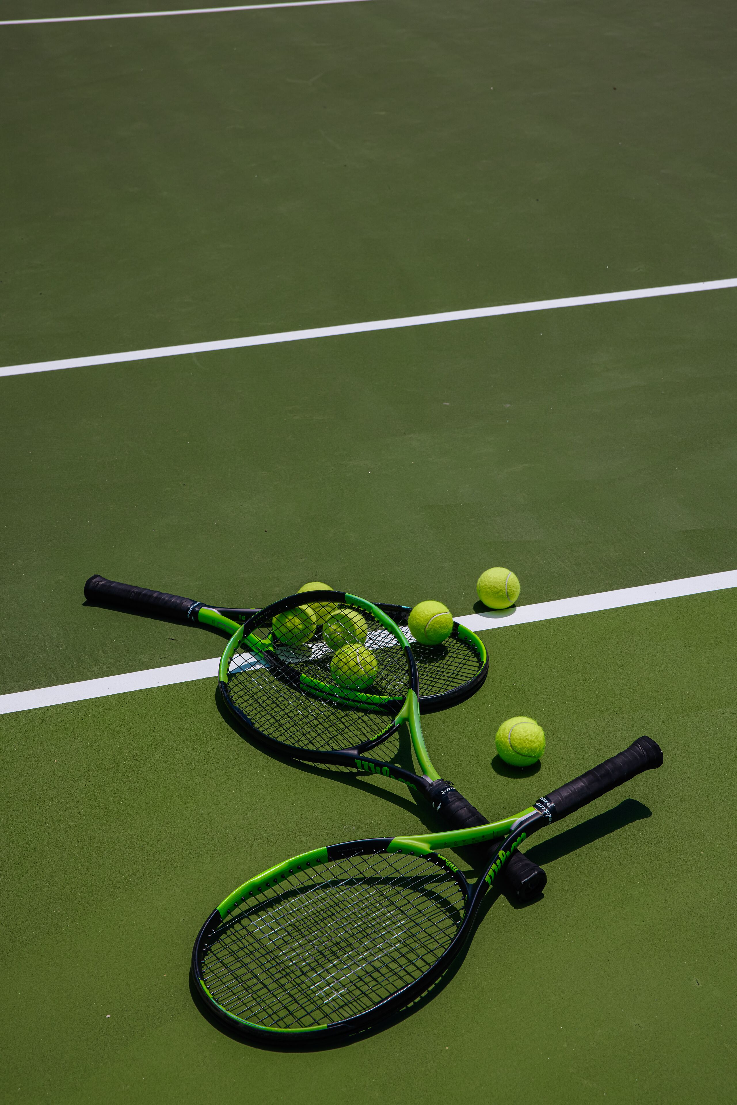Deux raquettes de tennis et plusieurs balles de tennis sur un terrain vert.