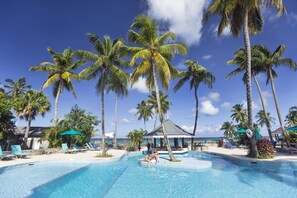 A pool area with palm trees, lounge chairs, and a view of the ocean.