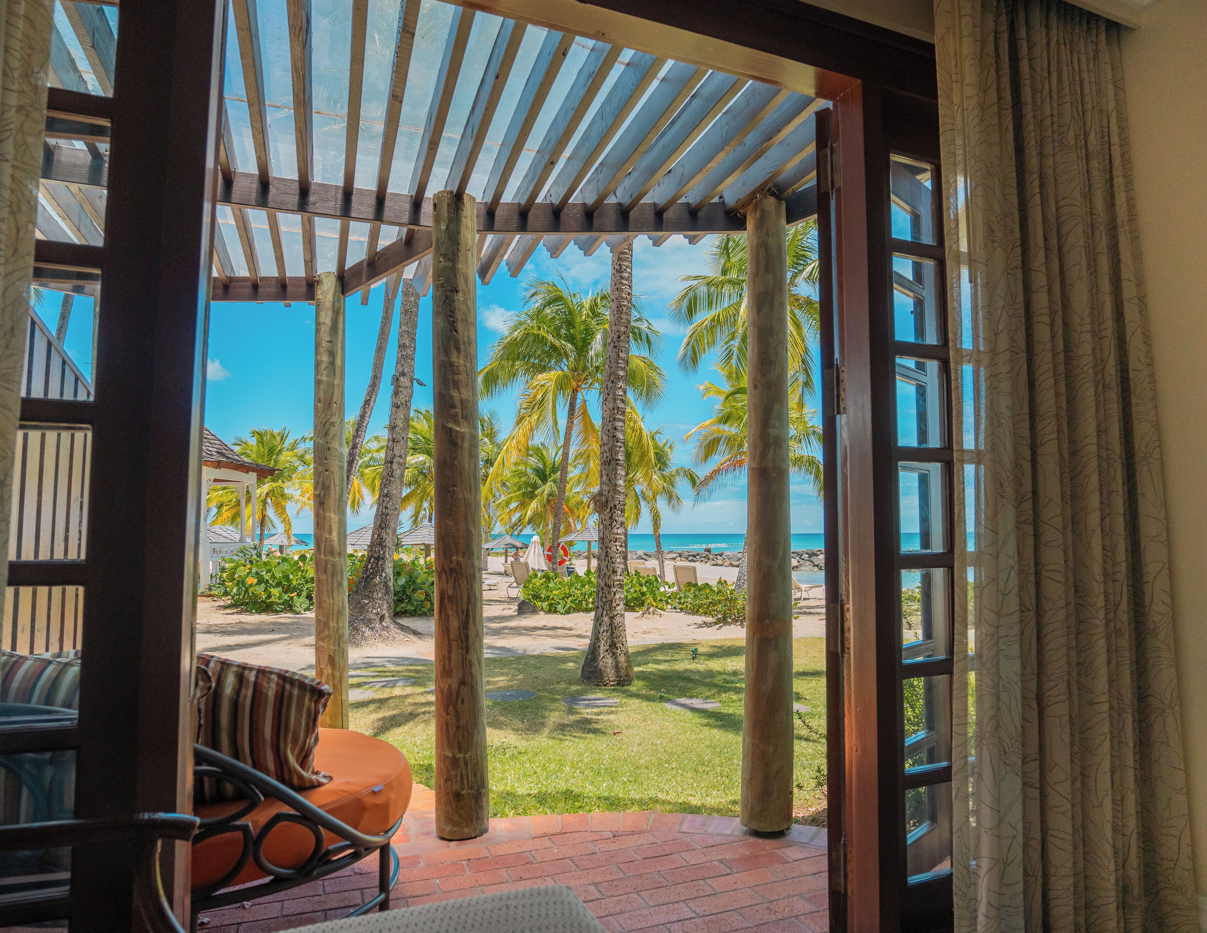 A covered outdoor seating area with a view of a beach and palm trees.