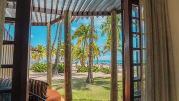 A covered outdoor seating area with a view of a beach and palm trees.