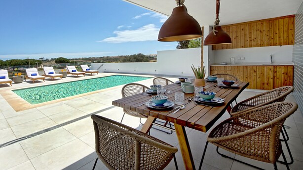 Una terraza en la azotea con piscina, mesa de comedor, sillas de mimbre e iluminación colgante.