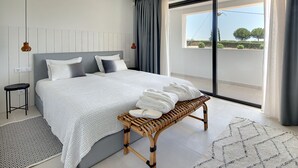 Un dormitorio moderno con una cama grande, un banco con toallas, un tapete estampado y vistas al exterior.