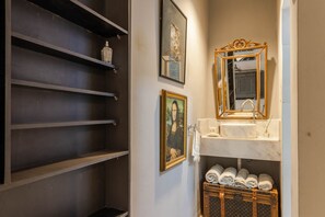 A bathroom with a marble sink, a gold-framed mirror, and a Louis Vuitton suitcase on a shelf.