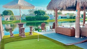 Un campo da golf con un putting green, poltrone in vimini e un padiglione con tetto di paglia.