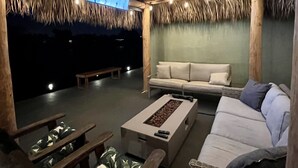 Zona relax esterna con mobili in legno, televisore a schermo piatto e luci decorative.