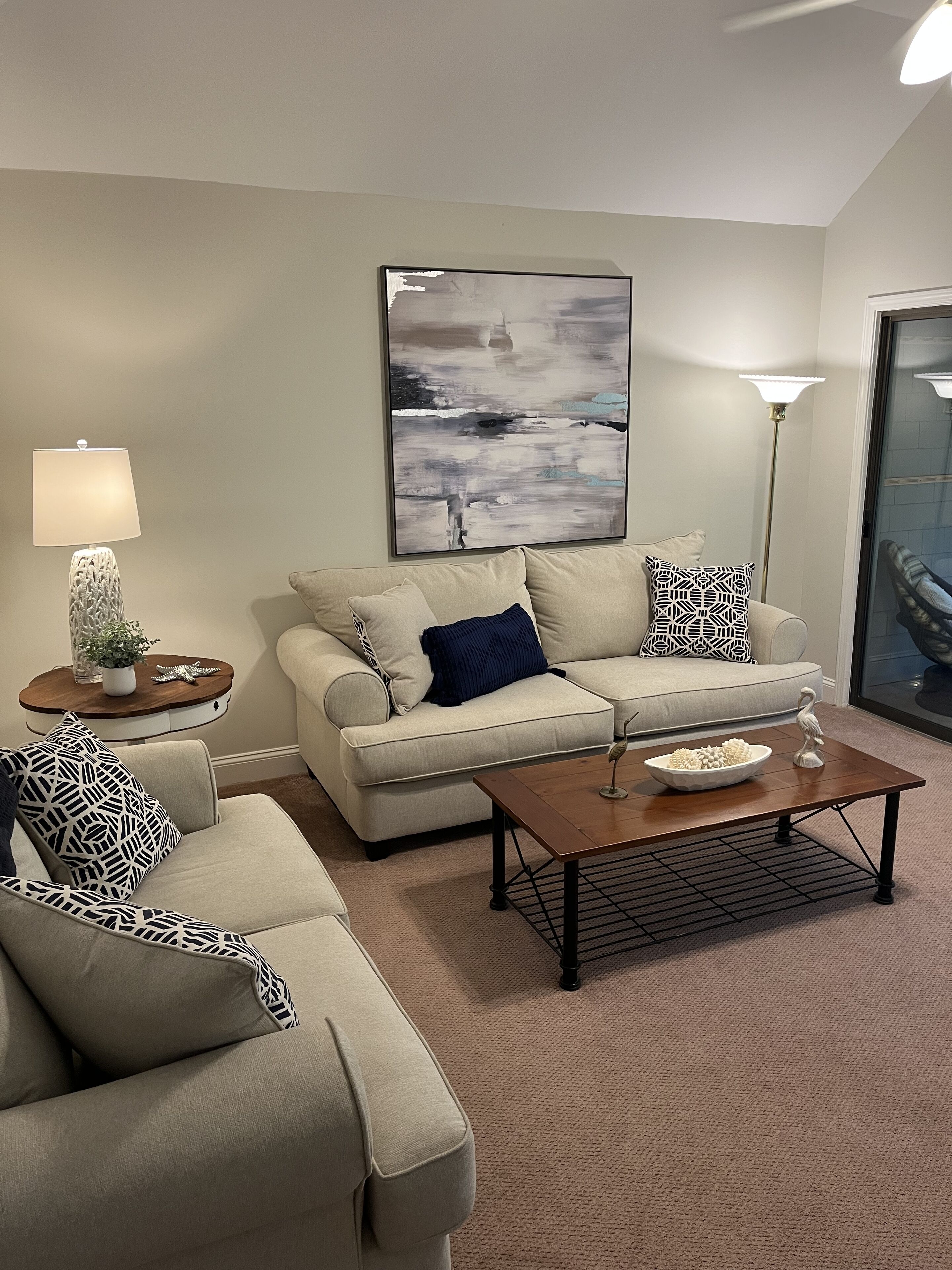 A living room with a beige sofa, a coffee table, a floor lamp, and a painting on the wall.