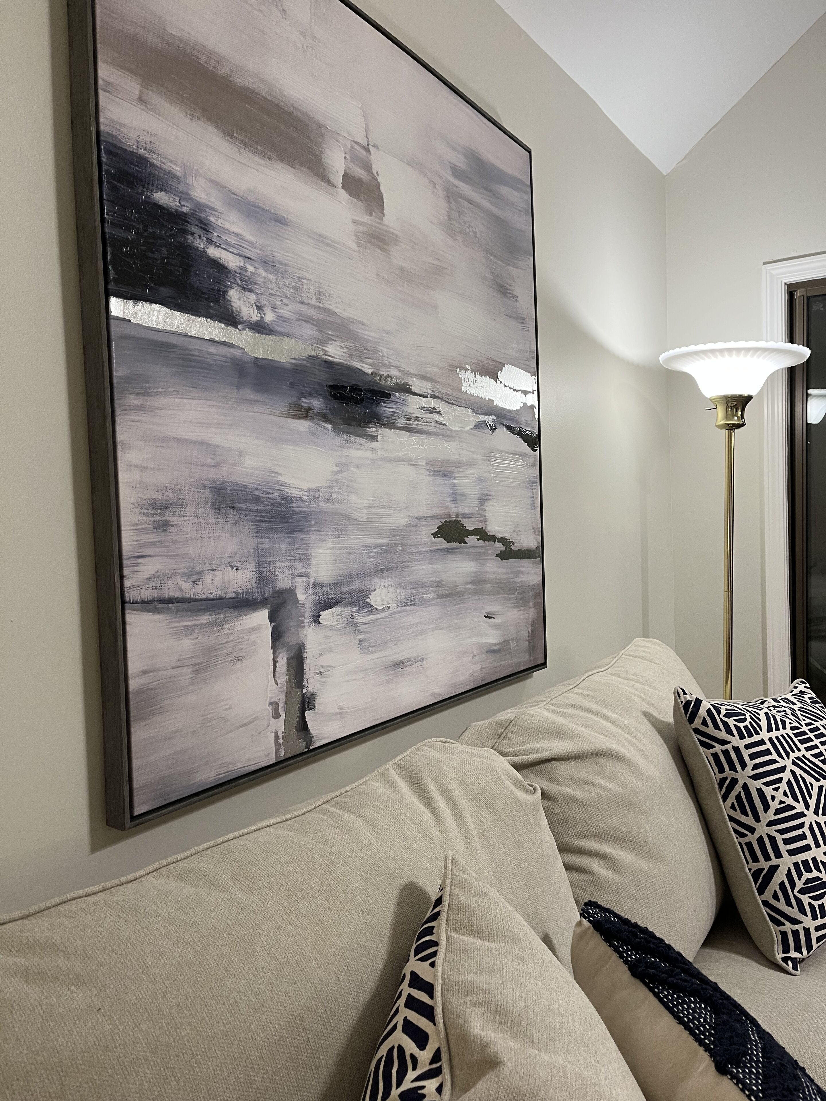 A living room with a large abstract painting, a floor lamp, and a sofa with patterned cushions.