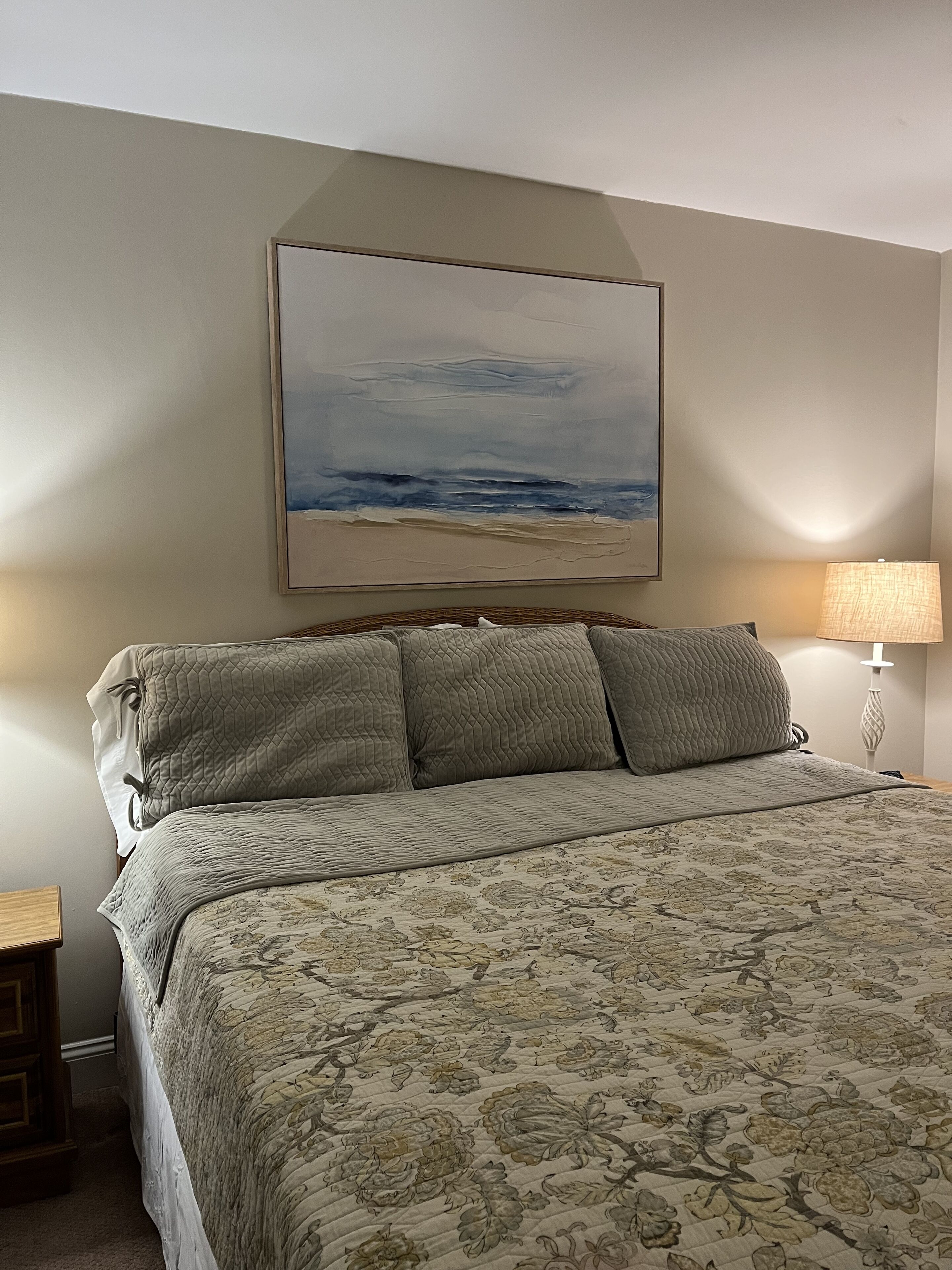Et soveværelse med seng, et maleri af en strandscene, en lampe og et natbord.