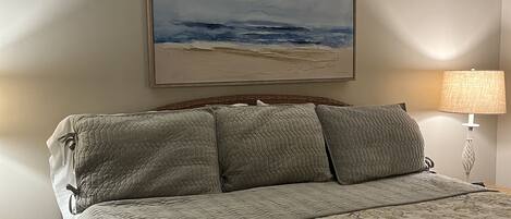 Et soveværelse med seng, et maleri af en strandscene, en lampe og et natbord.