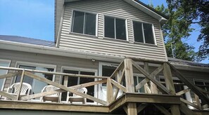 A two-story house with a wooden deck and white plastic chairs.